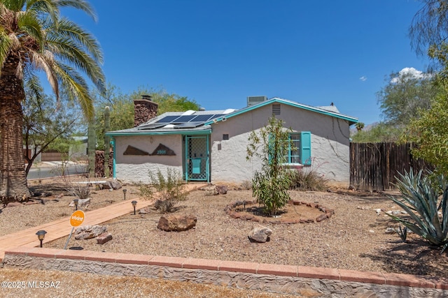 view of front of home featuring roof mounted solar panels, a chimney, stucco siding, and fence