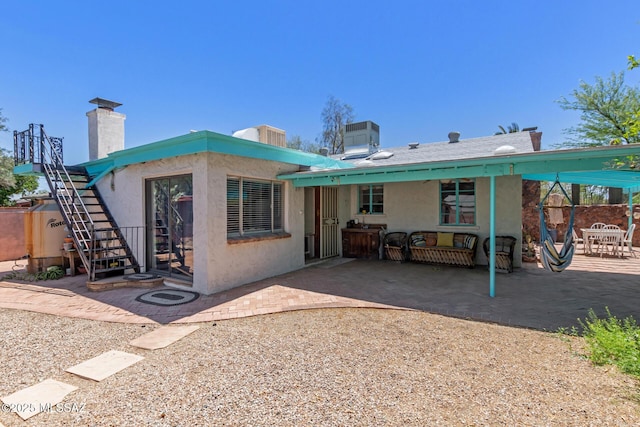 back of house featuring stucco siding, a patio, stairway, and a chimney