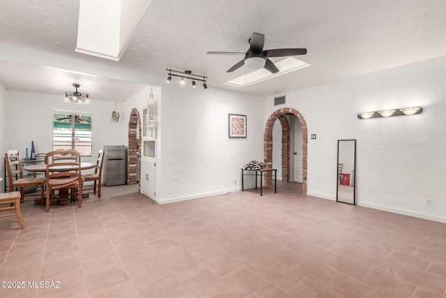 empty room with a skylight, a ceiling fan, arched walkways, and baseboards