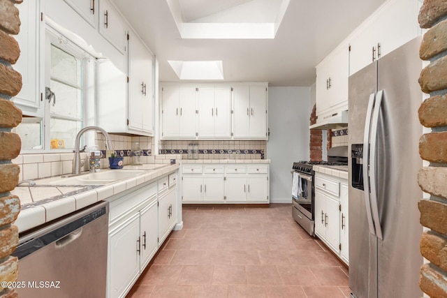 kitchen with appliances with stainless steel finishes, a skylight, decorative backsplash, white cabinetry, and tile countertops