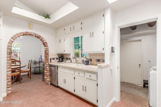 kitchen with a sink, dishwasher, backsplash, tile counters, and white cabinetry