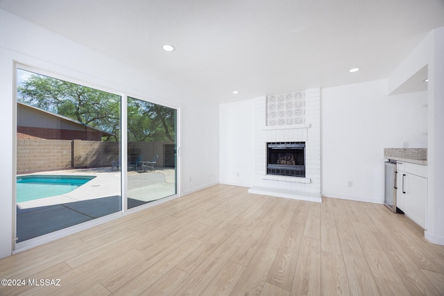 unfurnished living room featuring recessed lighting, light wood-style flooring, a brick fireplace, and baseboards