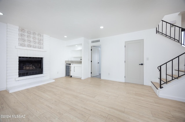 unfurnished living room featuring visible vents, stairs, a fireplace, beverage cooler, and light wood finished floors