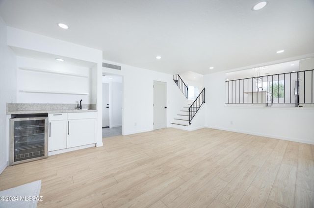 unfurnished living room with light wood finished floors, beverage cooler, indoor wet bar, stairs, and visible vents