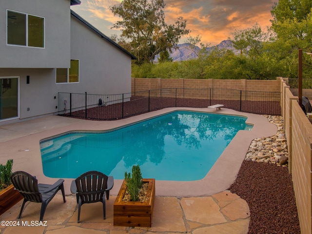 pool at dusk with a fenced in pool, a mountain view, a fenced backyard, and a patio area