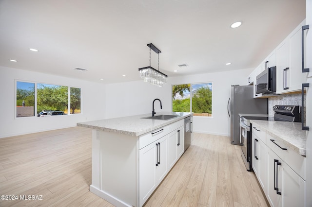 kitchen with a sink, appliances with stainless steel finishes, white cabinetry, and an island with sink