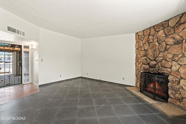 9770 E Hollow Pl, Tucson, AZ 85748 - unfurnished living room with a stone fireplace, a textured ceiling, visible vents, and dark tile patterned flooring