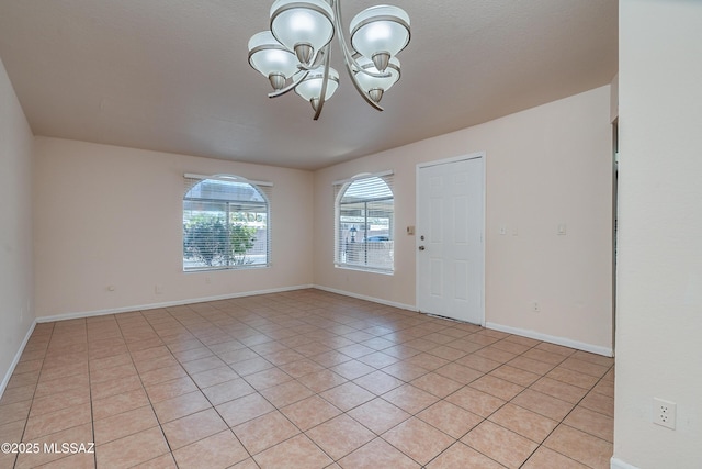 empty room with light tile patterned flooring, baseboards, and an inviting chandelier