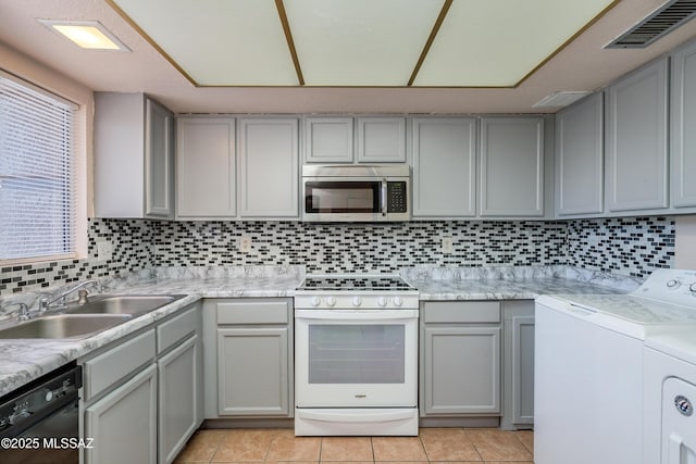 kitchen featuring washing machine and clothes dryer, a sink, stainless steel microwave, visible vents, and white range with gas stovetop