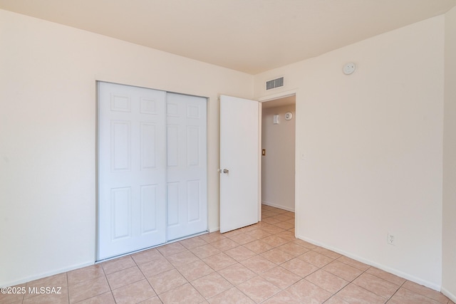 unfurnished bedroom with light tile patterned flooring, a closet, visible vents, and baseboards