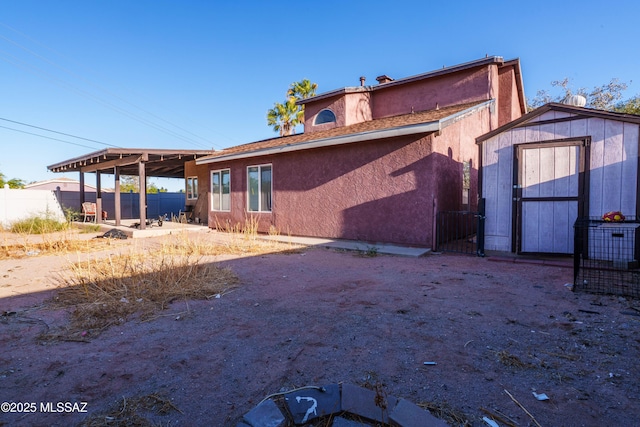 rear view of house with an outdoor structure, a storage unit, stucco siding, and fence