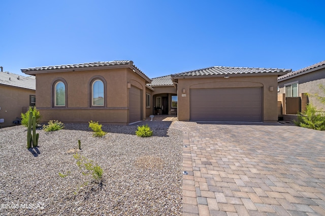 mediterranean / spanish-style house with stucco siding, decorative driveway, a tiled roof, and an attached garage