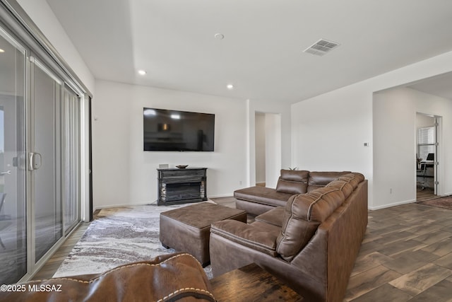 living room with recessed lighting, a glass covered fireplace, visible vents, baseboards, and wood finished floors
