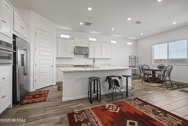 kitchen with visible vents, wood finished floors, under cabinet range hood, and high quality fridge