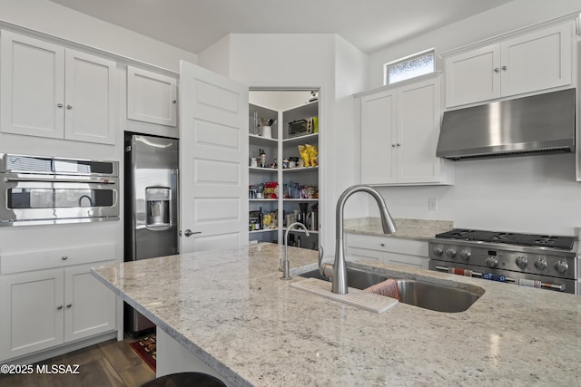 kitchen with light stone counters, stainless steel appliances, white cabinets, a sink, and ventilation hood