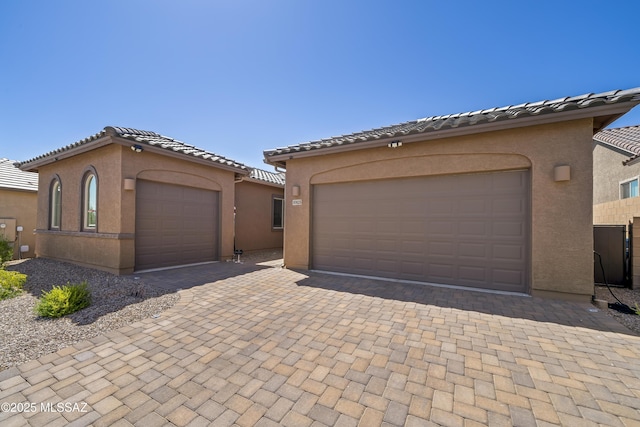 mediterranean / spanish house with stucco siding, decorative driveway, a tiled roof, and a garage