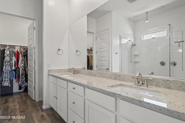 full bath featuring wood finished floors, a tile shower, double vanity, and a sink