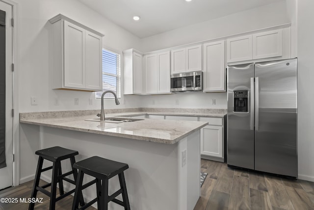 kitchen featuring a kitchen breakfast bar, white cabinetry, a sink, stainless steel appliances, and a peninsula