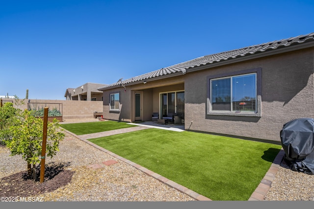 back of house featuring a tile roof, a patio, a lawn, stucco siding, and fence