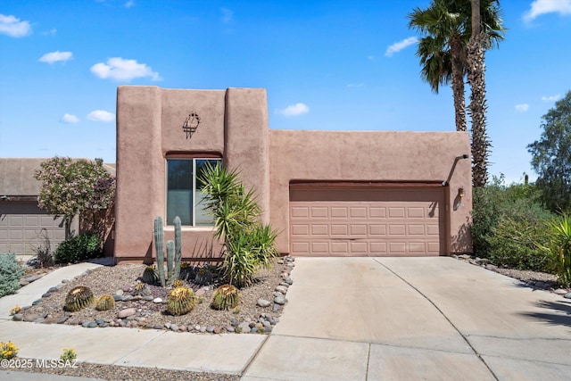 pueblo-style house with stucco siding, driveway, and a garage