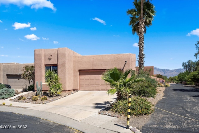 pueblo-style home featuring concrete driveway, a garage, a mountain view, and stucco siding