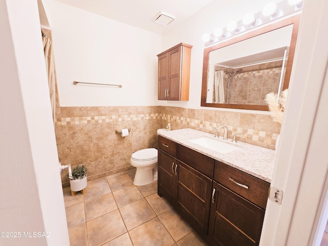 full bathroom with tile patterned floors, toilet, vanity, tile walls, and wainscoting