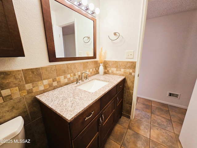 bathroom featuring tile patterned floors, toilet, vanity, tile walls, and wainscoting