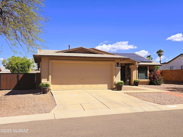 ranch-style house featuring solar panels, concrete driveway, fence, an attached garage, and stucco siding