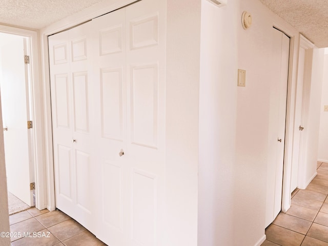 hall with a textured ceiling and light tile patterned floors