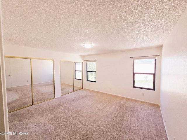 unfurnished bedroom featuring carpet, a textured ceiling, and two closets