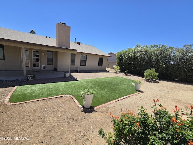 back of property with stucco siding, a lawn, a chimney, and a patio