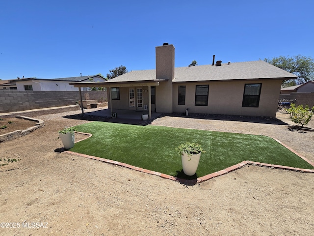 rear view of house with a chimney, a fenced backyard, a yard, stucco siding, and a patio