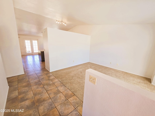 tiled empty room with vaulted ceiling, track lighting, carpet floors, french doors, and baseboards