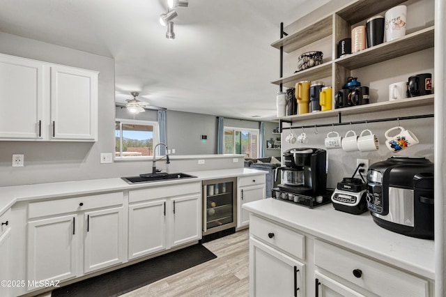 kitchen featuring wine cooler, a ceiling fan, a sink, light wood-style floors, and a peninsula