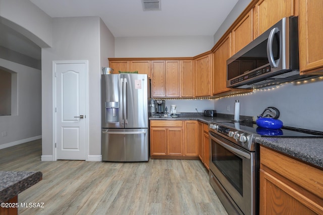 kitchen featuring visible vents, brown cabinetry, dark countertops, light wood finished floors, and appliances with stainless steel finishes