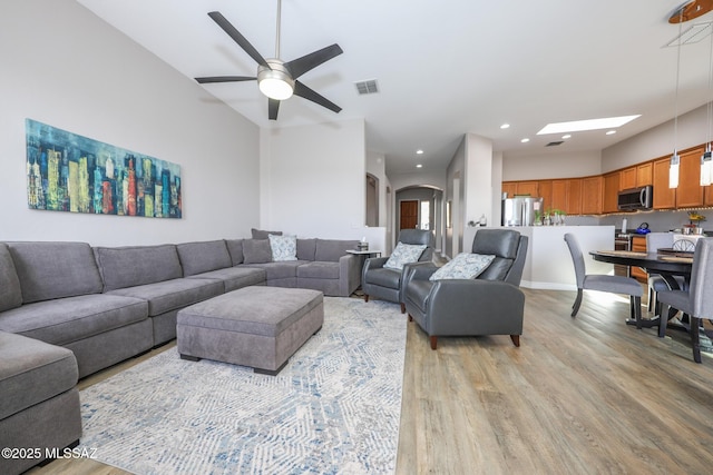 living room with light wood-style floors, arched walkways, a ceiling fan, and visible vents