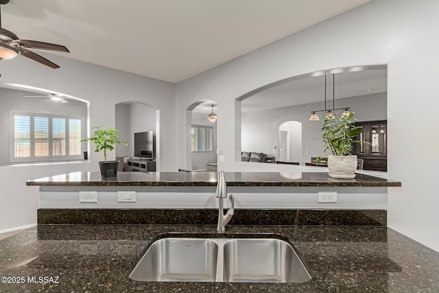 kitchen with dark stone countertops, a ceiling fan, open floor plan, and a sink