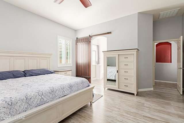 bedroom with a barn door, ceiling fan, light wood-type flooring, visible vents, and baseboards