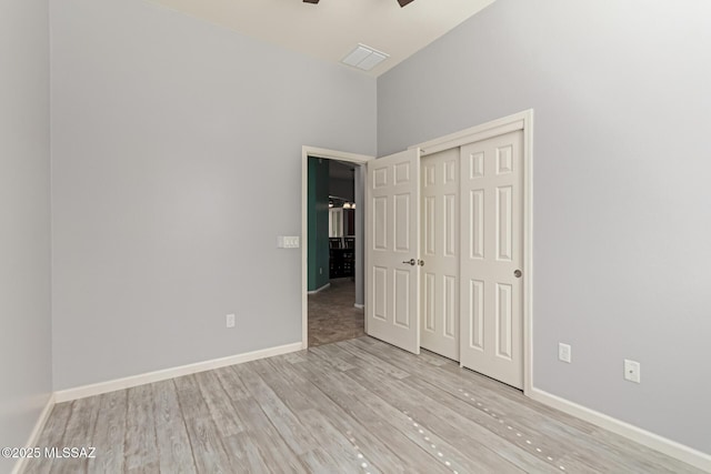 unfurnished bedroom featuring a towering ceiling, visible vents, baseboards, and light wood-style floors