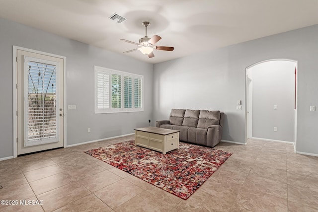 living area featuring visible vents, baseboards, arched walkways, light tile patterned flooring, and a ceiling fan