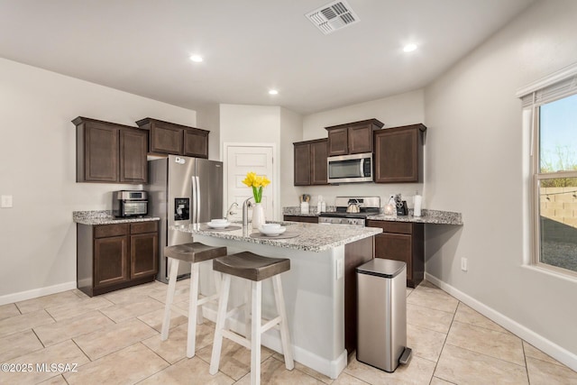 17949 S Whispering Glen Path, Sahuarita, AZ 85629 - kitchen featuring appliances with stainless steel finishes, dark brown cabinetry, a center island with sink, light stone counters, and recessed lighting