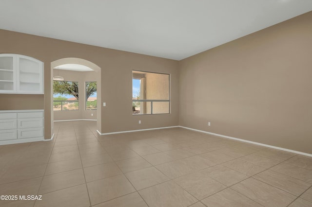 38876 S Serenity Ln, Tucson, AZ 85739 - empty room featuring arched walkways, baseboards, and light tile patterned flooring