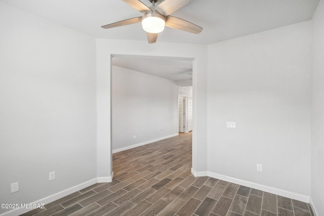 empty room featuring a ceiling fan, baseboards, and dark wood-style floors