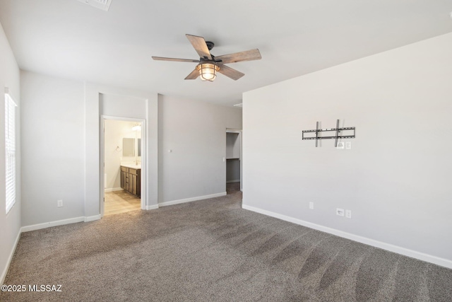 unfurnished bedroom with a ceiling fan, light carpet, connected bathroom, a walk in closet, and baseboards