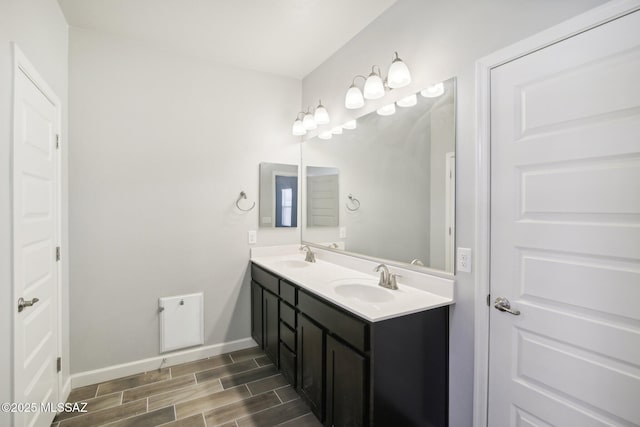 bathroom with baseboards, wood finish floors, a sink, and double vanity