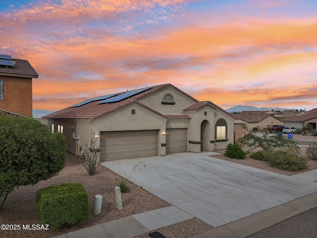 mediterranean / spanish house featuring concrete driveway, a tiled roof, an attached garage, roof mounted solar panels, and stucco siding