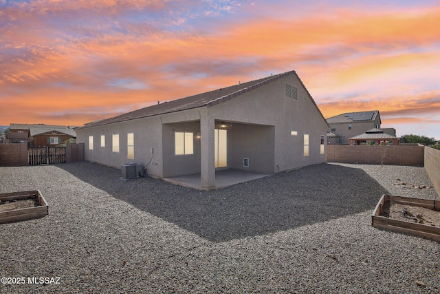 rear view of property with a vegetable garden, a fenced backyard, central air condition unit, stucco siding, and a patio