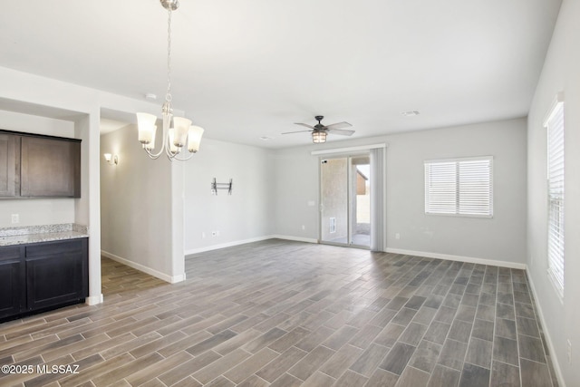 unfurnished living room with wood finished floors, baseboards, and ceiling fan with notable chandelier