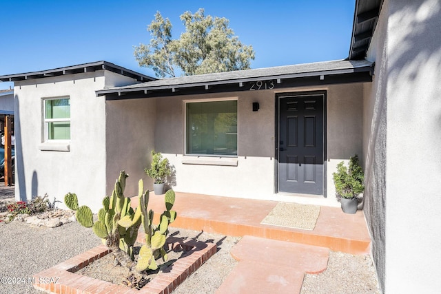 property entrance with roof with shingles and stucco siding