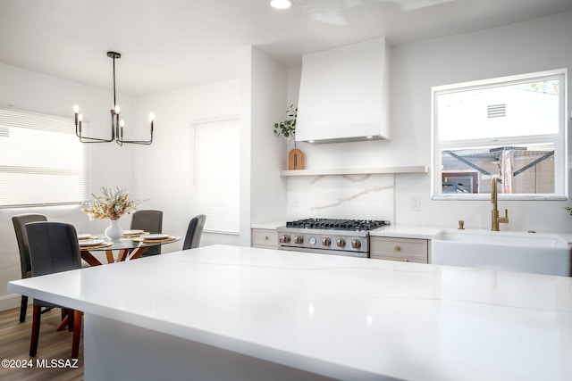 kitchen with a sink, a notable chandelier, custom range hood, light countertops, and range